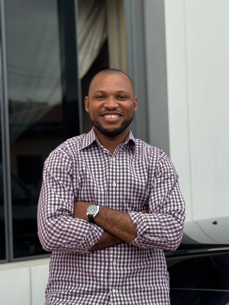 Chukwuemeka Kalu smiling in a checked shirt, with his arms folded.